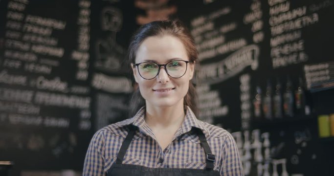 Woman barista standing behind the bar counter in coffee shop and looking at camera