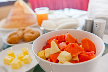 Cut fruits in white bowl on a dinning table. 