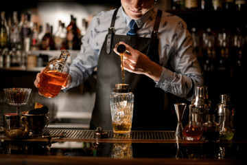 bartender holds bottle with drink and pours liquid into shaker.