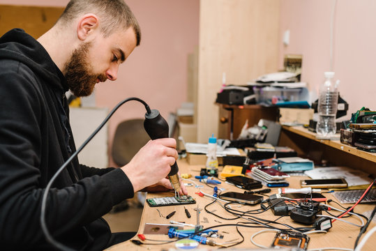 The technician repairing the smartphone motherboard in the lab. Concept of computer hardware, mobile phone, electronic, repairing, upgrade, technology. Man showing process of phone repair in workshop.