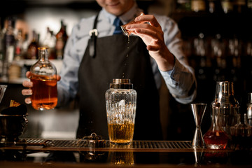 Glassy shaker with drink and ice stands on bar counter.