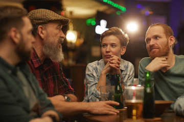 Group of people talking to each other while sitting at the table with beer and alcohol drinks in the pub