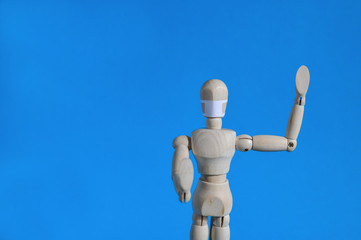 A figure of a man made of wood in a medical mask holds his hands up, warning of danger. Coronavirus, pandemic and epidemic concept