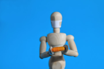 A wooden figure in a medical mask holds an orange pill on a blue background. Coronavirus, pandemic and epidemic concept