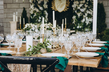 banquet wooden tables are decorated with compositions of candles and greens, on the tables are plates with napkins, glasses and cutlery. wedding, holiday