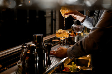 barman gently pours finished cold brown cocktail from glass shaker into wineglass.
