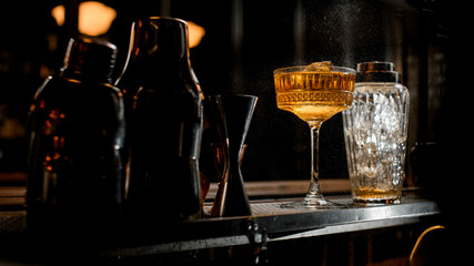 Glassy shaker and wineglass of brown alcoholic drink stand at bar