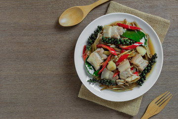 top view of stir fried sizzle pork belly in a ceramic dish on wooden table. asian homemade style food concept.