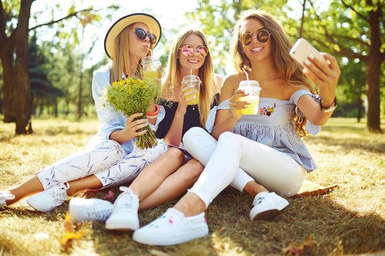 Three fashion young girls laugh and make selfies in hot summer day. Friends enjoy their vacation have fun together. Summer concept.