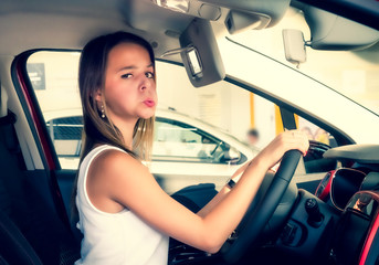 Nice girl sitting in the new car in the showroom. Buying new cars concept. beautiful young woman grimacing sad looking at camera