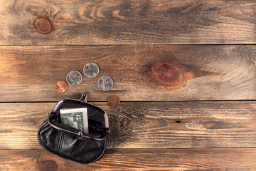 Open black leather pocket wallet with coins one cent, quarter dollar and 2 dollars banknote nearby. Financial crisis, poverty, lack money. On wooden background or table. Flat lay. Top view.