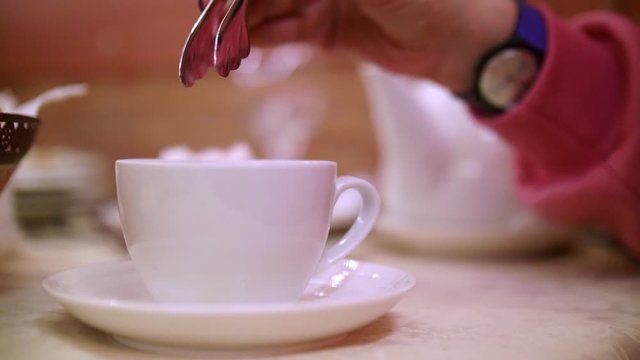Close up of woman's hands putting piece of suger into bowl of tea. Tea drinking ceremony.