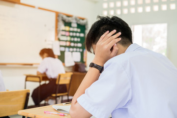 stressed headaches, Asian boy student studying for test or exams in classroom, learning lessons doing final exam at high school with Thailand uniform in class room. Education system concept.