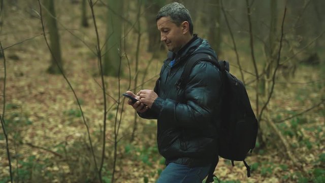 Close up man uses smarphone walk smile look around feel happy technology park cellphone autumn traveller tree telephone mobile phone casual slow motion