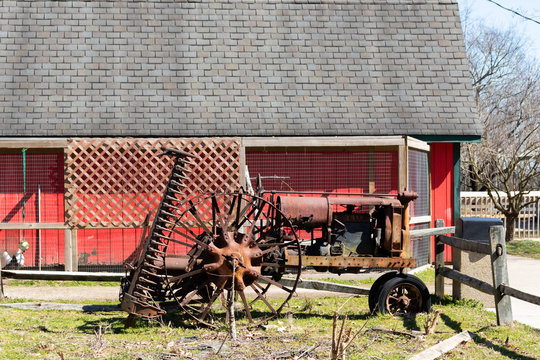 A rusty old tractor placed beside a larger red barn in a public park.