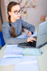 Beautiful young school girl left-handed working at home in her room with a laptop and class notes studying in a virtual class. Distance education and learning concept during quarantine