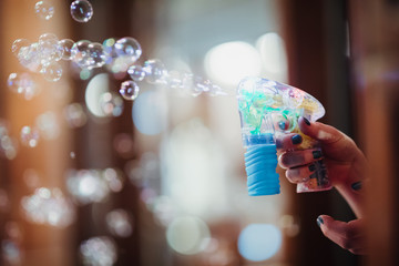 A man's hand uses a bubble gun to blow bubbles