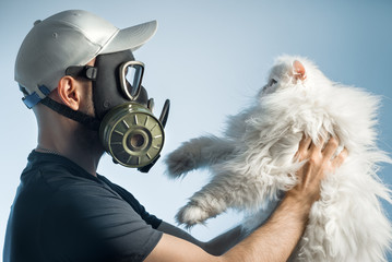 A man in a gas mask holds a cat. The man is allergic to pets.