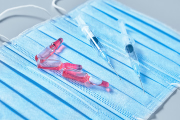 Surgical mask for cover mouth and nose and red vaccine, syringe on gray background. Concept of protection, virus epidemic or pandemic, corona virus, covid-19