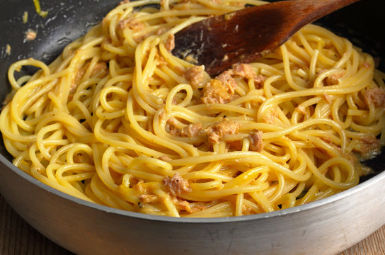 Spaghetti alla carbonara di tonno con uovo e pepe cotti in un tegame di alluminio antiaderente.