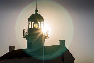 A lens flare bursts off the top of the Old Point Loma Lighthouse, towering above San Diego Bay in San Diego, California.