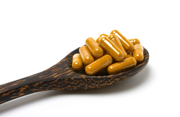 Turmeric (curcumin) capsules( Herbal capsule) in a wooden spoon isolated on white background.