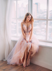 Happy beautiful girl with mysterious smile closed eyes sits elegantly on windowsill, blurred city...