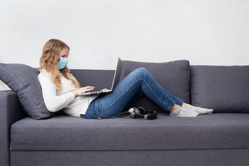 Woman in a respiratory mask working home sitting on a sofa with a laptop. Stay home, quarantine concept