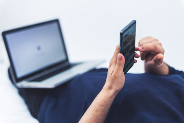 close up view of a man using his mobile phone and a lap top while lying on bed