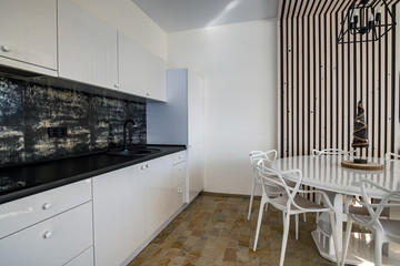 Interior of modern spacious kitchen with white walls, decorative wooden elements, contemporary furniture and big soft couch.