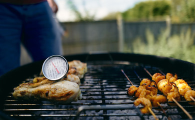 A food thermometer checking that chicken is being cooked correctly, safely on a barbecue along with...