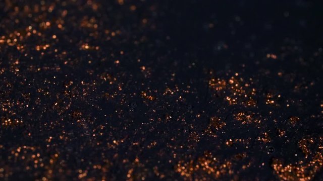 Abstract colorful red golden sand organically flows in colorful liquid in macro, black background