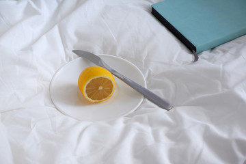 lemon on a platter and Notepad, in a white bed. Coziness. Minimalism.