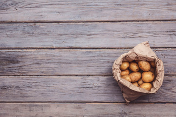 A paper bag full of fresh homegrown potatoes on a wooden background