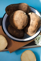  Unwashed potatoes in a white bowl on a blue background. Photo for food markets, a menu for vegetarians.