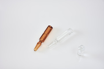 Clear and brown glass ampoules with medicine laying on white acrylic table next to open clear glass ampoule standing upright 