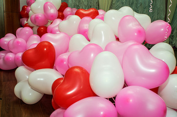 A large number of inflated multicolored heart-shaped balloons are stacked in bulk in the corner of the room for the upcoming holiday, close-up, copy space.