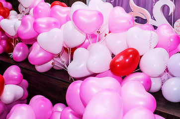 A large number of inflated multicolored heart-shaped balloons are stacked in bulk in the corner of the room for the upcoming holiday, close-up, copy space, toned.