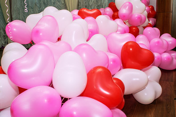 A large number of inflated multicolored heart-shaped balloons are stacked in bulk in the corner of the room for the upcoming holiday, close-up, copy space, toned.