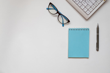 Computer keyboard, glasses, notepad and pen on a white surface. Work on remote access, study online, home office, shopping online concept. View from above. Horizontal orientation. Copy Space.