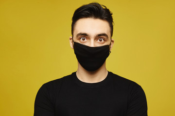 Handsome man in black t-shirt and black protective mask isolated on yellow background. Healthy lifestyle concept, seasonal illness, and seasonal flu concept.