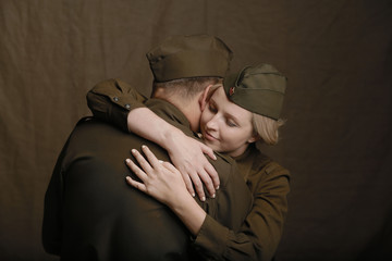 Young couple in love in world war Second military uniform hugs as if saying goodbye on brown...
