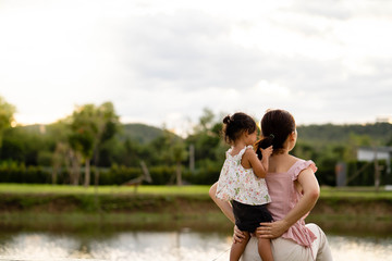 Naklejka premium Mother and daughter sitting at pond looking at beautiful landscape. 