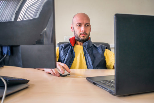 The man works at several server computers in the office. The specialist is sitting in a chair in front of two displays. An office worker looks at the laptop screen. 