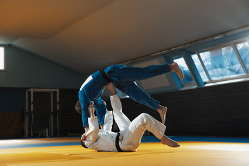 Two young judo caucasian fighters in white and blue kimono with black belts training martial arts...