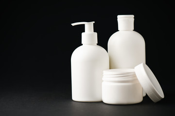 Fototapeta na wymiar container with face cream near white bottles on black