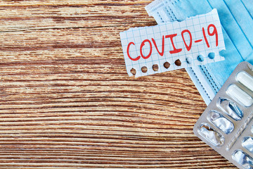 Fototapeta na wymiar Inscription COVID-19 near the medical mask with pills on the wooden background with copy space. Concept of protection from Coronavirus. Closeup
