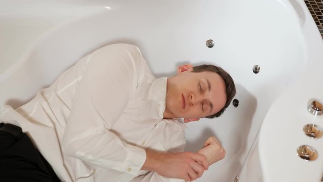 man in trousers and a shirt is lying in a bath with an epileptic seizure.