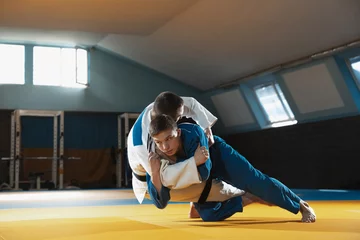 Keuken foto achterwand Two young judo caucasian fighters in white and blue kimono with black belts training martial arts in the gym with expression, in action, motion. Practicing fighting skills. Overcoming, reaching target © master1305