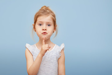 a little girl with light hair on a blue isolated background. Emotions of surprise. Hand gesture